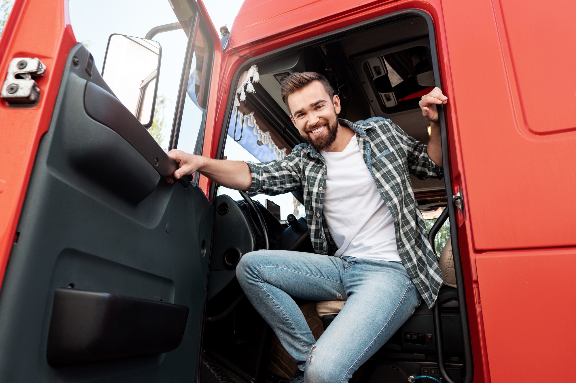 Young smiling male truck driver inside his red cargo truck